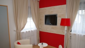 Un salon moderne avec un mur d’accent rouge, un téléviseur à écran plat fixé au-dessus d’un panneau en bois et une lampe rouge.