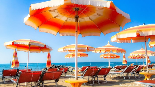 Una playa con hileras de sombrillas de rayas rojas y blancas y sillas reclinables rojas.