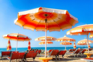 Una playa con hileras de sombrillas de rayas rojas y blancas y sillas reclinables rojas.