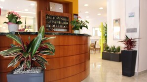 Una zona de recepción con mostrador de madera, plantas en macetas y suelo de baldosas.