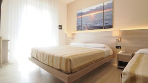 Una habitación de hotel moderna con una cama grande, mesitas de noche, una lámpara de pared y un cuadro de una puesta de sol sobre el agua.