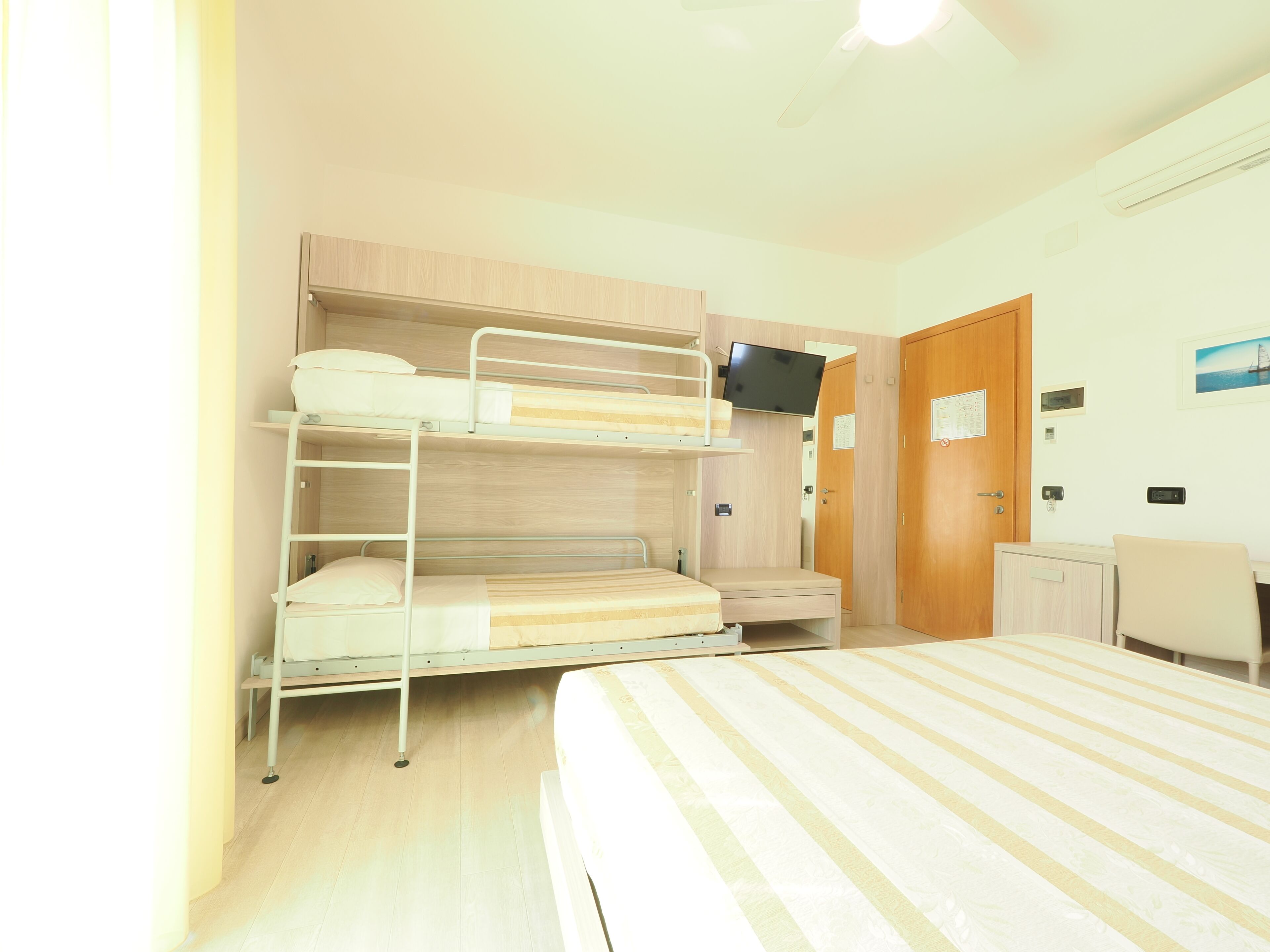 Une chambre avec un lit superposé, une télévision, un bureau et une porte.