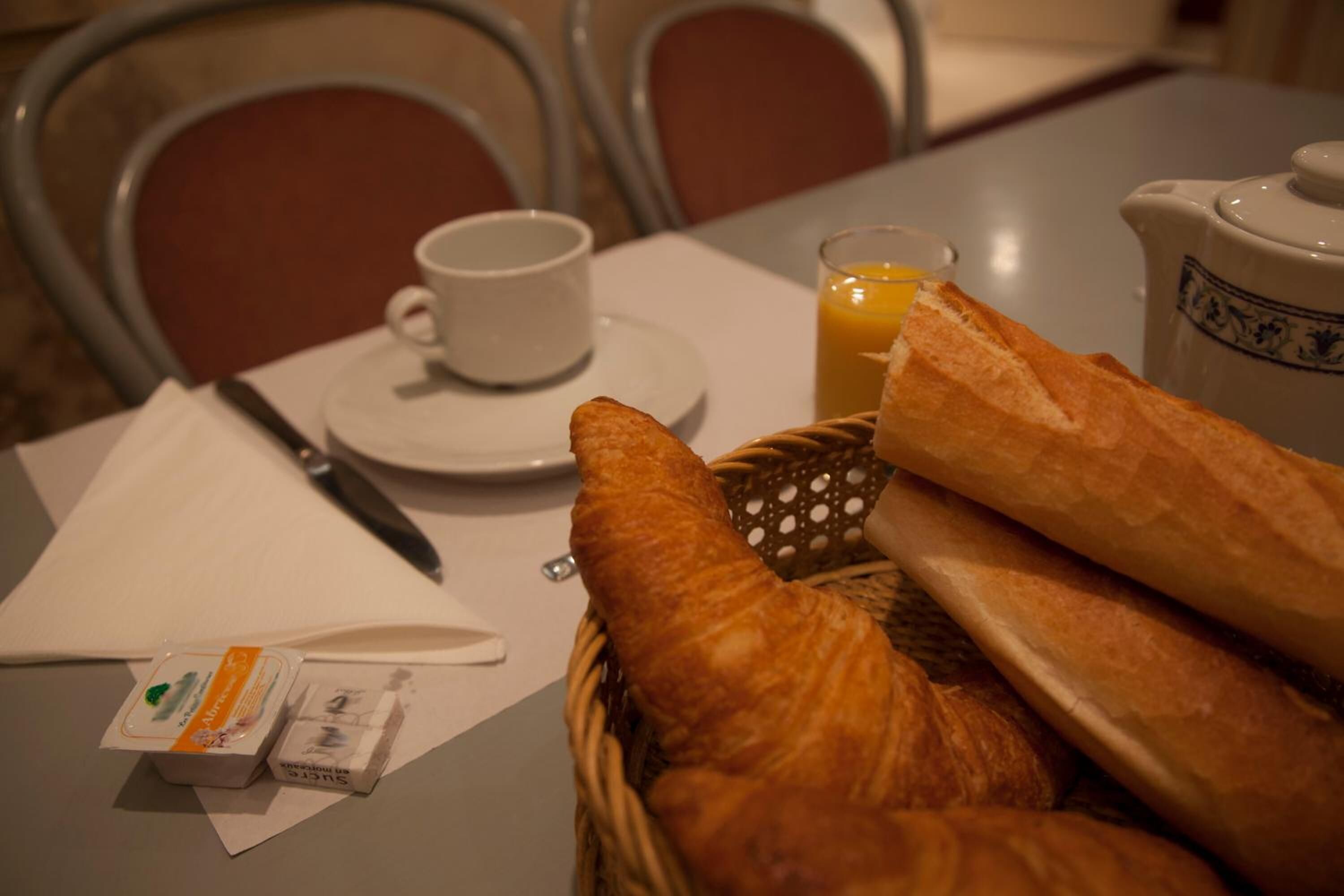 A breakfast setting with bread, a cup, and a glass of orange juice on a table.