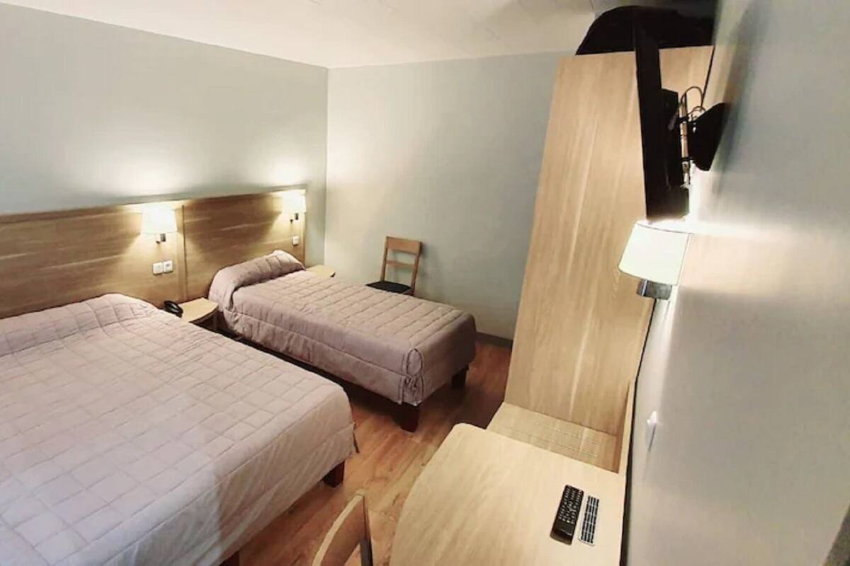 A hotel room with two beds, bedside tables, lamps, and a wooden headboard.
