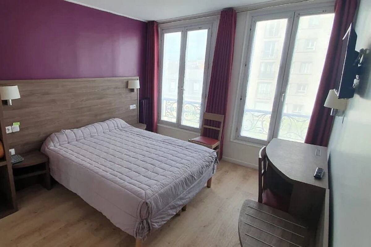 A bedroom with a bed, a wardrobe, a desk, and a window with curtains.