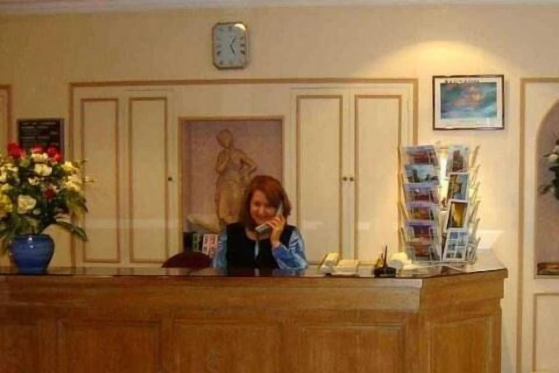 A reception desk with a clock, a statue, and a flower arrangement.