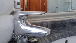 A bathroom with a marble sink, a chrome faucet, and a wooden door in the background. - Hotel Sablón (Llanes)