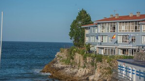 A coastal hotel with a restaurant, featuring a stone facade, multiple windows, and flags. - Hotel Sablón (Llanes)