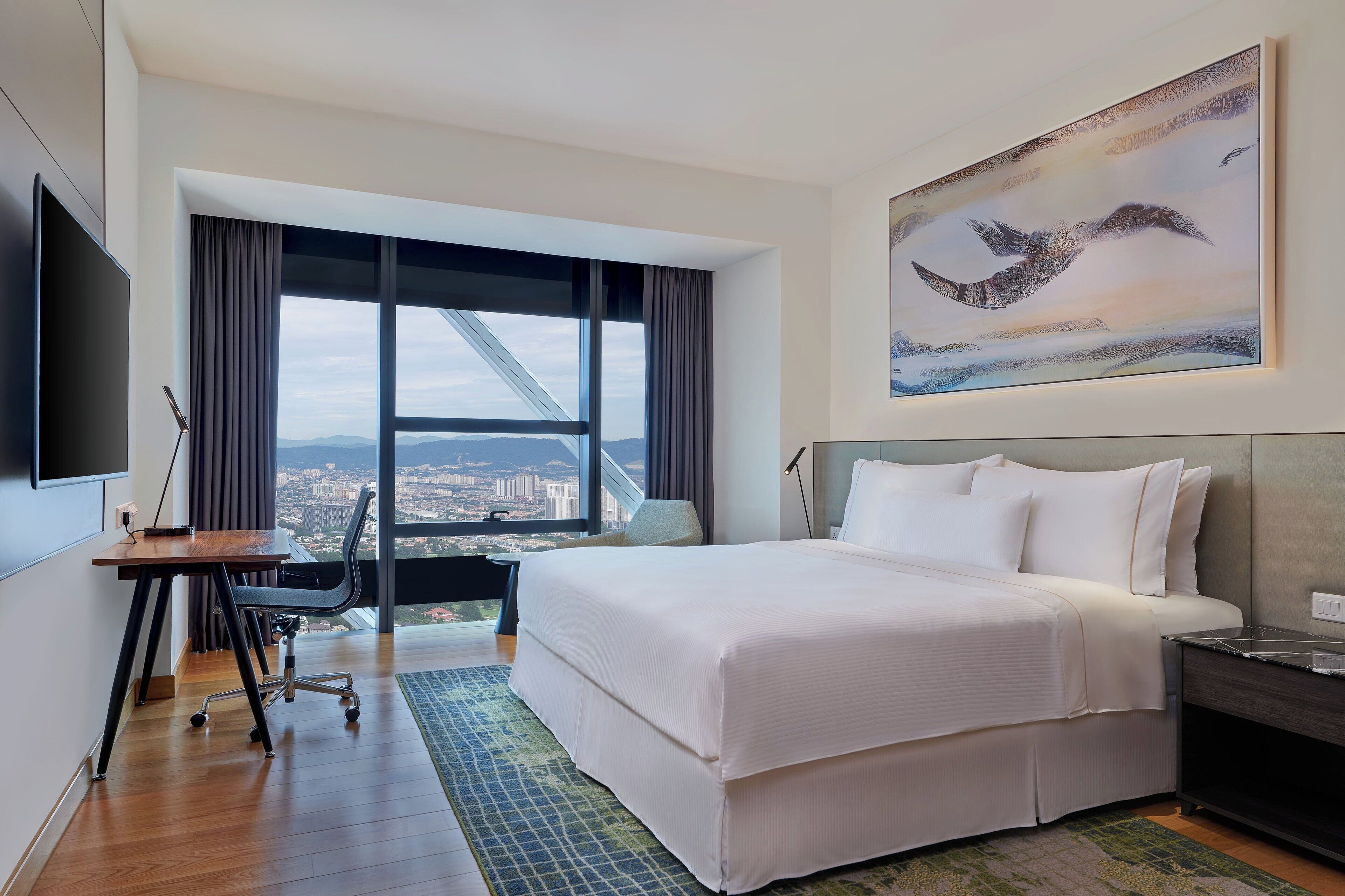 Habitación de hotel con una cama grande, un escritorio, una silla, un televisor y un cuadro de pájaros.