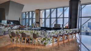 A modern bar area with a marble countertop, bar stools, and a city view through large windows. - Element by Marriott Kuala Lumpur (Kuala Lumpur)