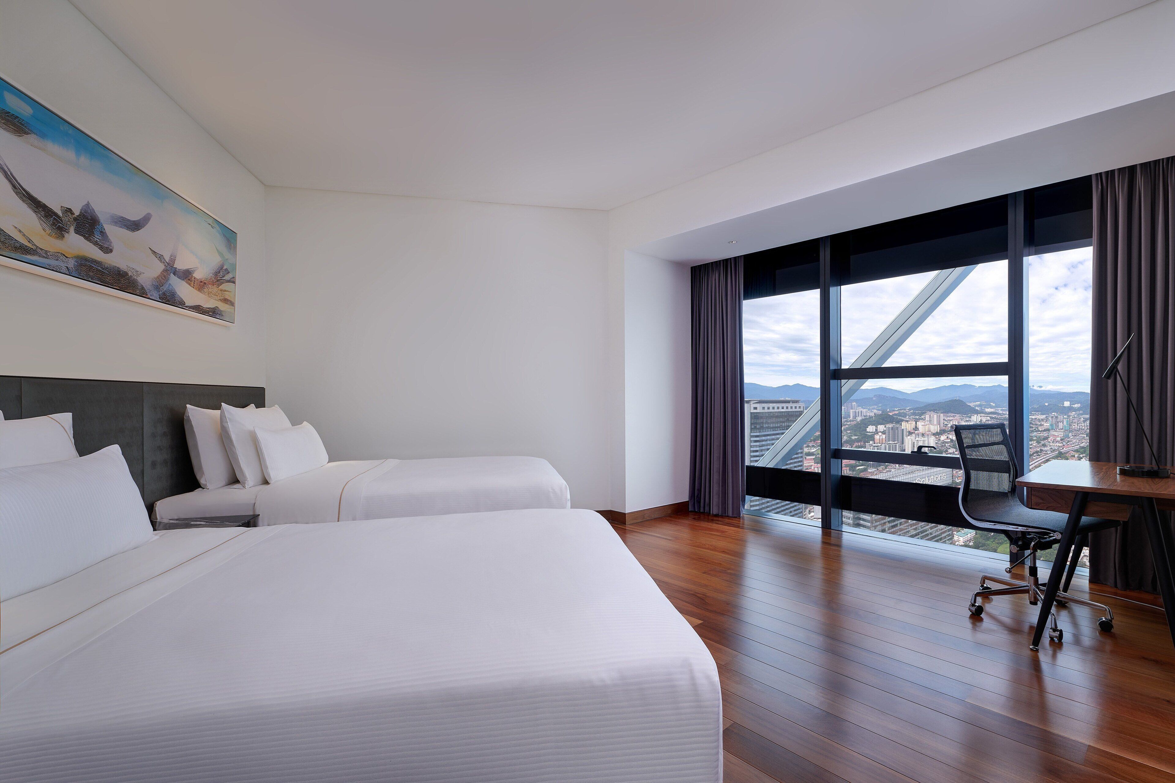 Camera d'albergo con due letti, una scrivania e un'ampia finestra con vista sulla città.