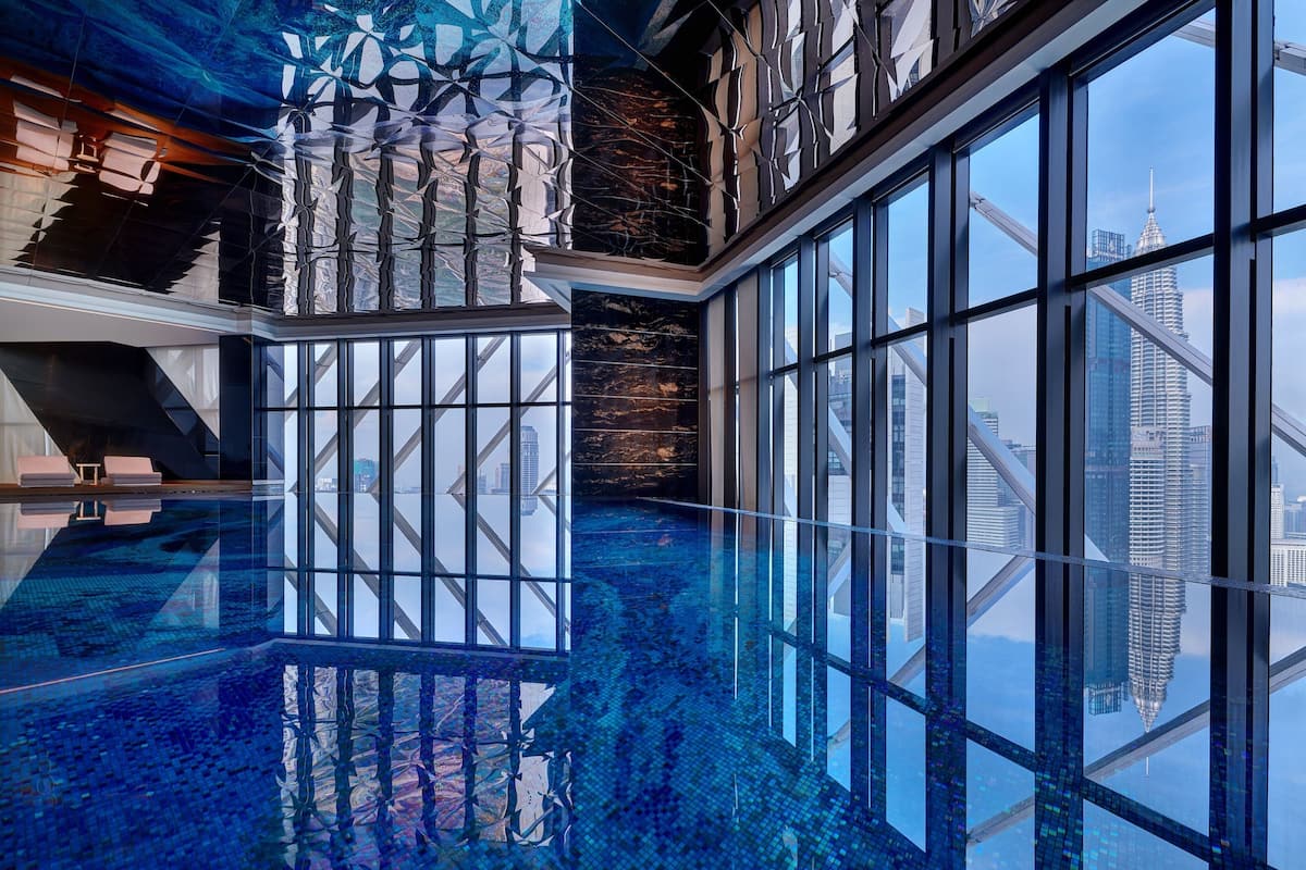 A modern hotel interior with a glass-bottomed pool reflecting the city skyline, large windows, and contemporary design elements.