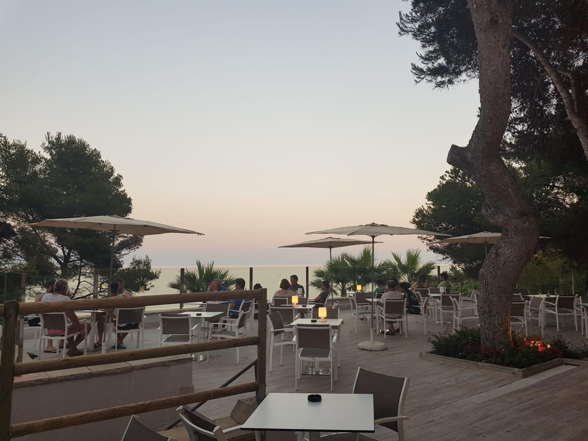An outdoor dining area with tables and chairs, umbrellas, and a view of the sea.
