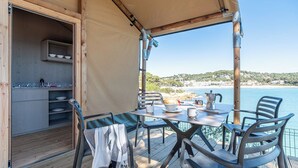A covered outdoor dining area with a table, chairs, and a view of the sea.