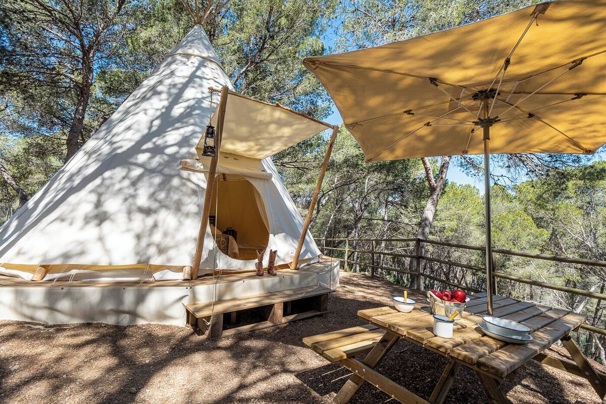 Une tente conique avec un banc en bois et une table de pique-nique équipée de bols et de tasses.