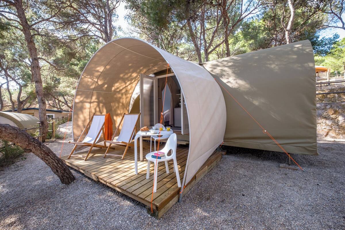 Une tente en forme de dôme dotée d’une terrasse en bois, de deux chaises blanches, d’une petite table et d’une fenêtre.