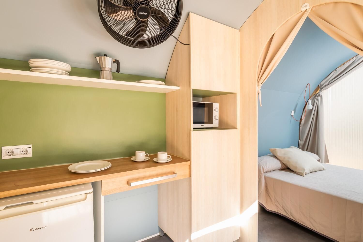 A compact kitchenette with a microwave, a fan, and a small dining area with plates and cups.