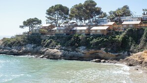 A coastal hotel with multiple wooden cabins, a rocky shoreline, and trees in the background.