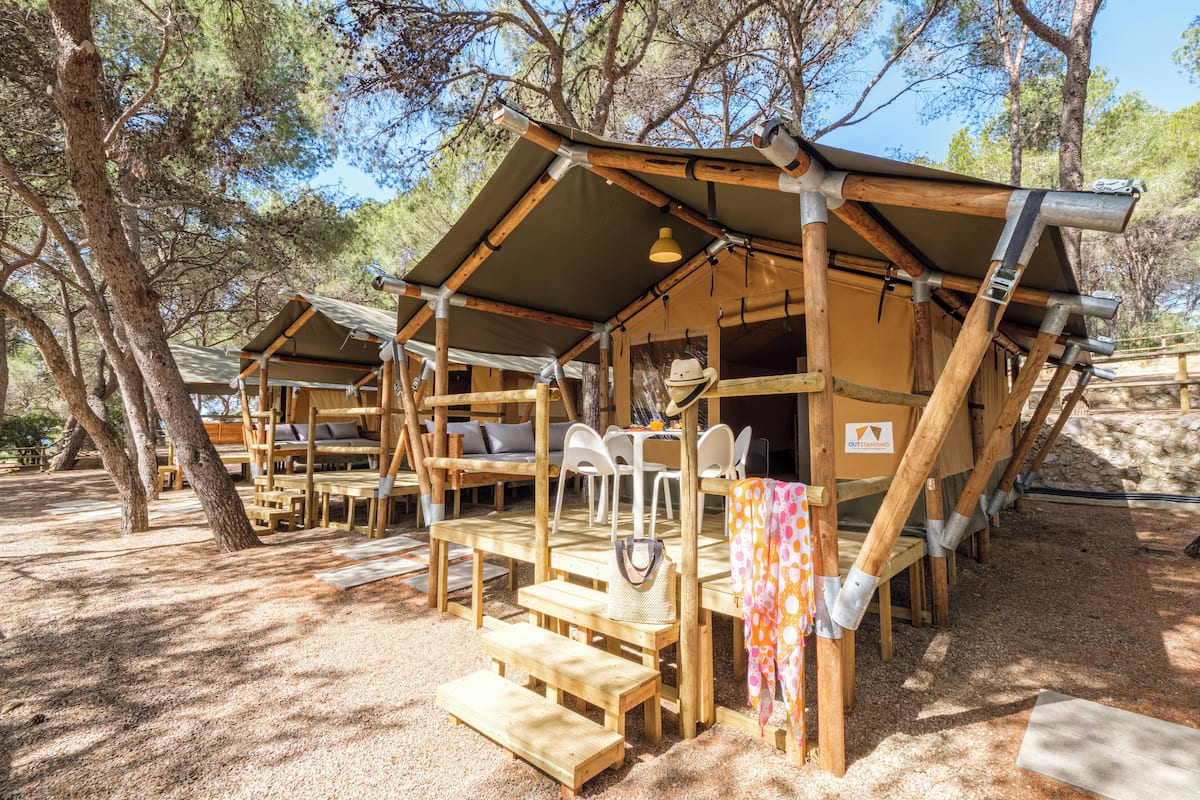 Un chalet rustique en bois doté d’un patio couvert, de meubles d’extérieur et offrant une vue sur la forêt environnante.