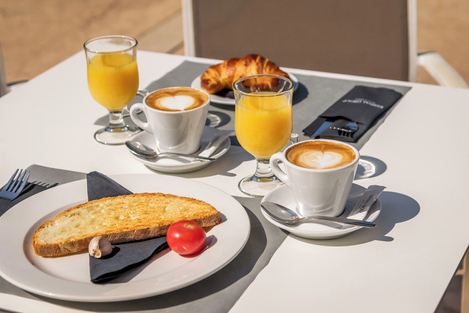 Een ontbijt met croissants, koffie, sinaasappelsap, toast en een tomaat op een witte tafel.