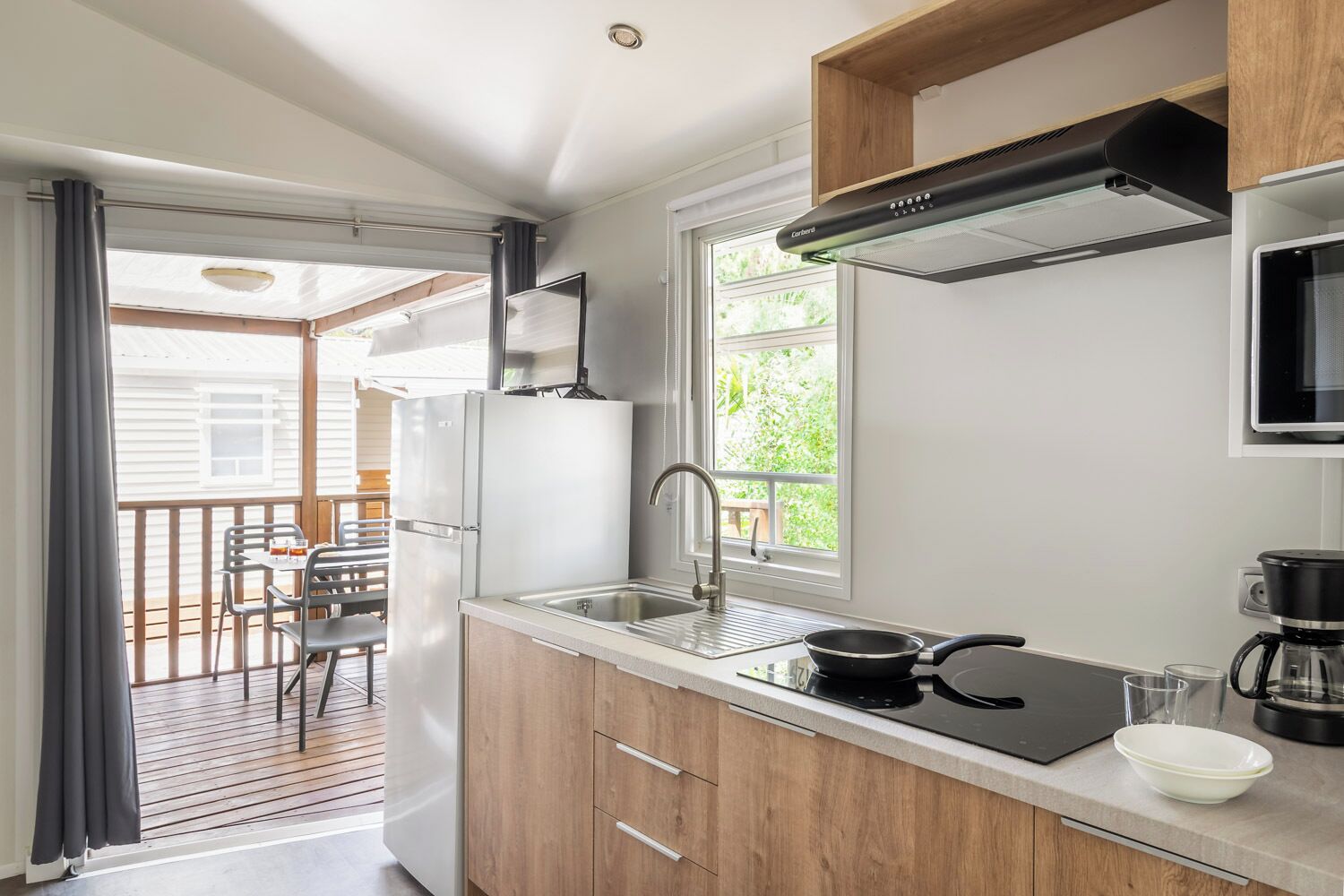 Una cocina compacta con un lavamanos, estufa y microondas. Se ve un comedor con sillas y una mesa a través de una puerta abierta.