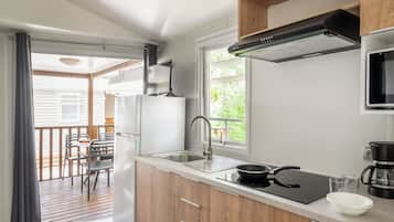 Una cocina compacta con un lavamanos, estufa y microondas. Se ve un comedor con sillas y una mesa a través de una puerta abierta.
