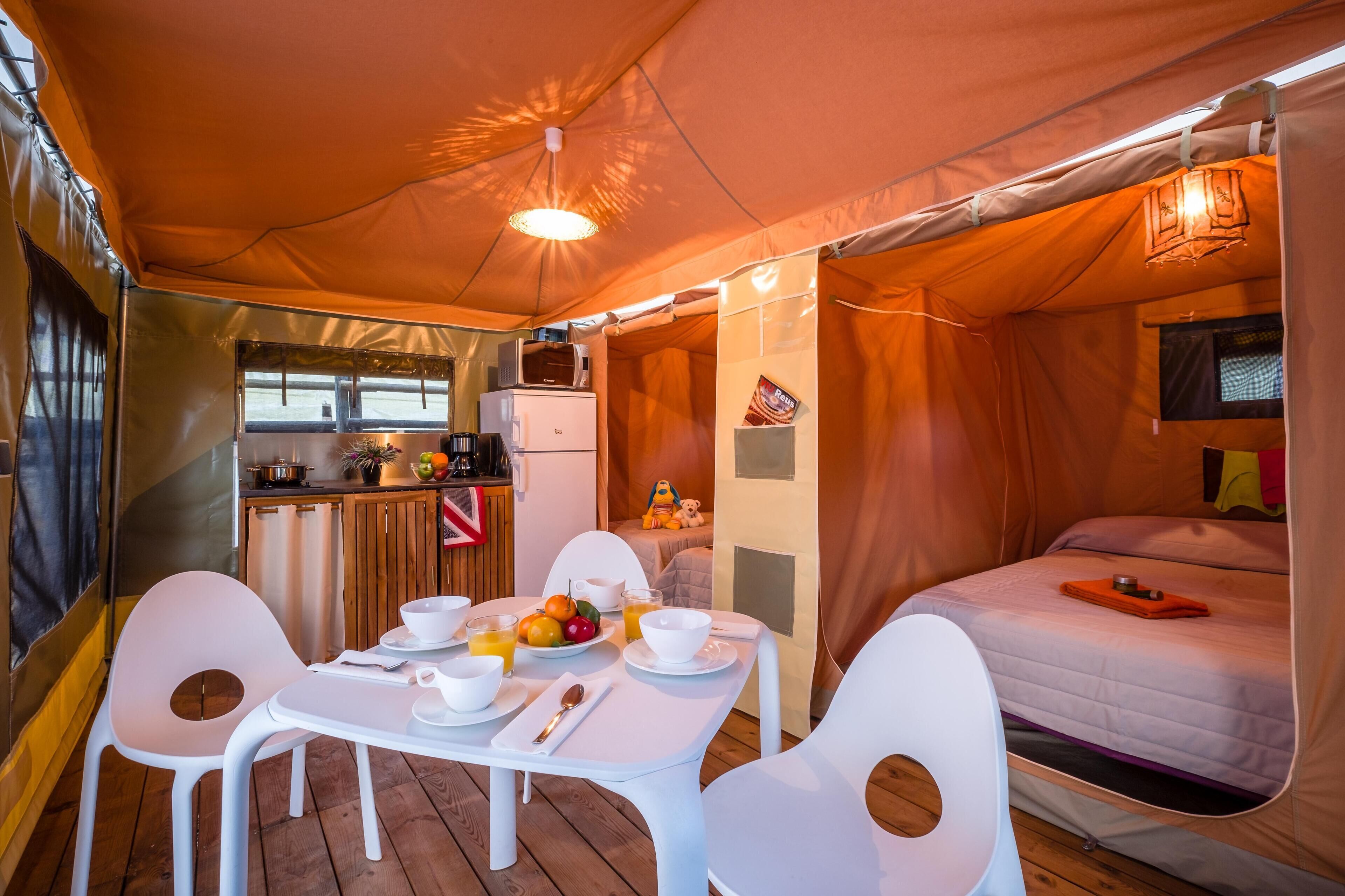 Allotjament en tenda amb zona de menjador, cuina americana i llit.
