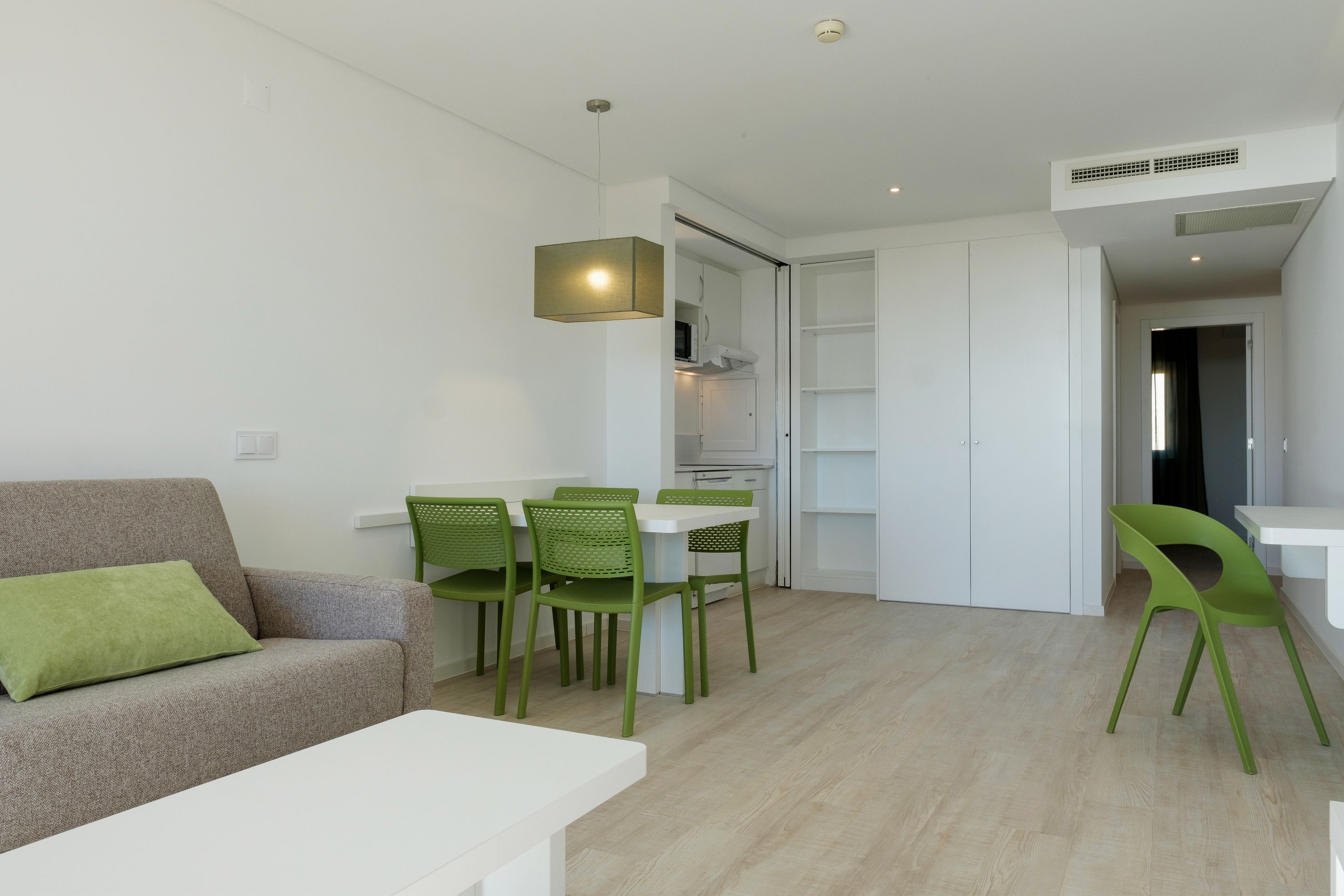 Een moderne woonkamer met een bank, een eettafel met stoelen, en een keuken met kasten en een magnetron.