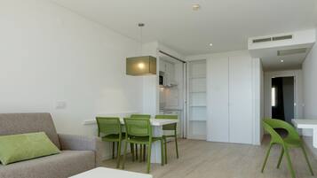 Een moderne woonkamer met een bank, een eettafel met stoelen, en een keuken met kasten en een magnetron.