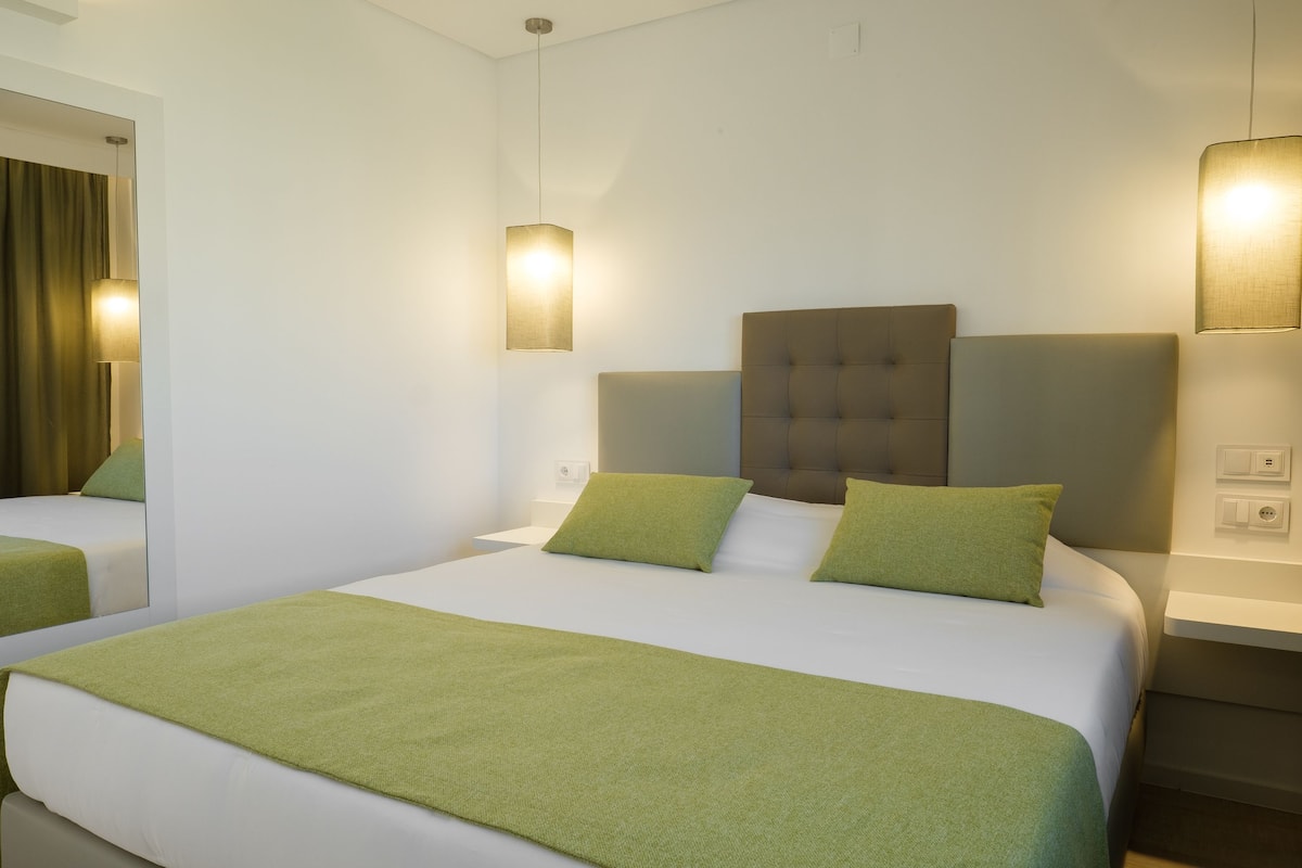 Camera d'albergo con un letto grande, due comodini, uno specchio e due lampade a parete.