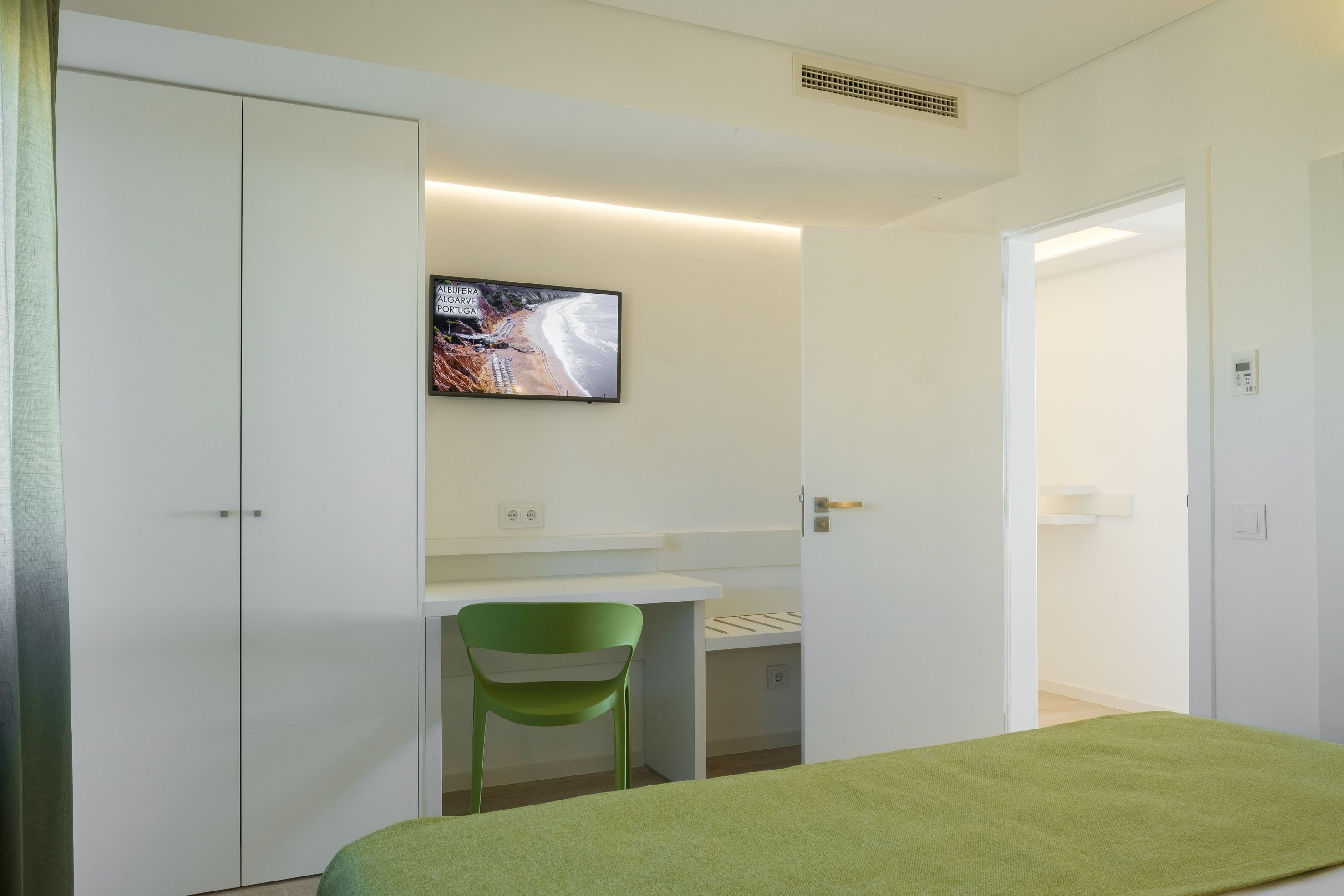 Ein Schlafzimmer mit einem Bett, einem Schreibtisch mit Stuhl, einem an der Wand montierten Fernseher und einem Kleiderschrank.