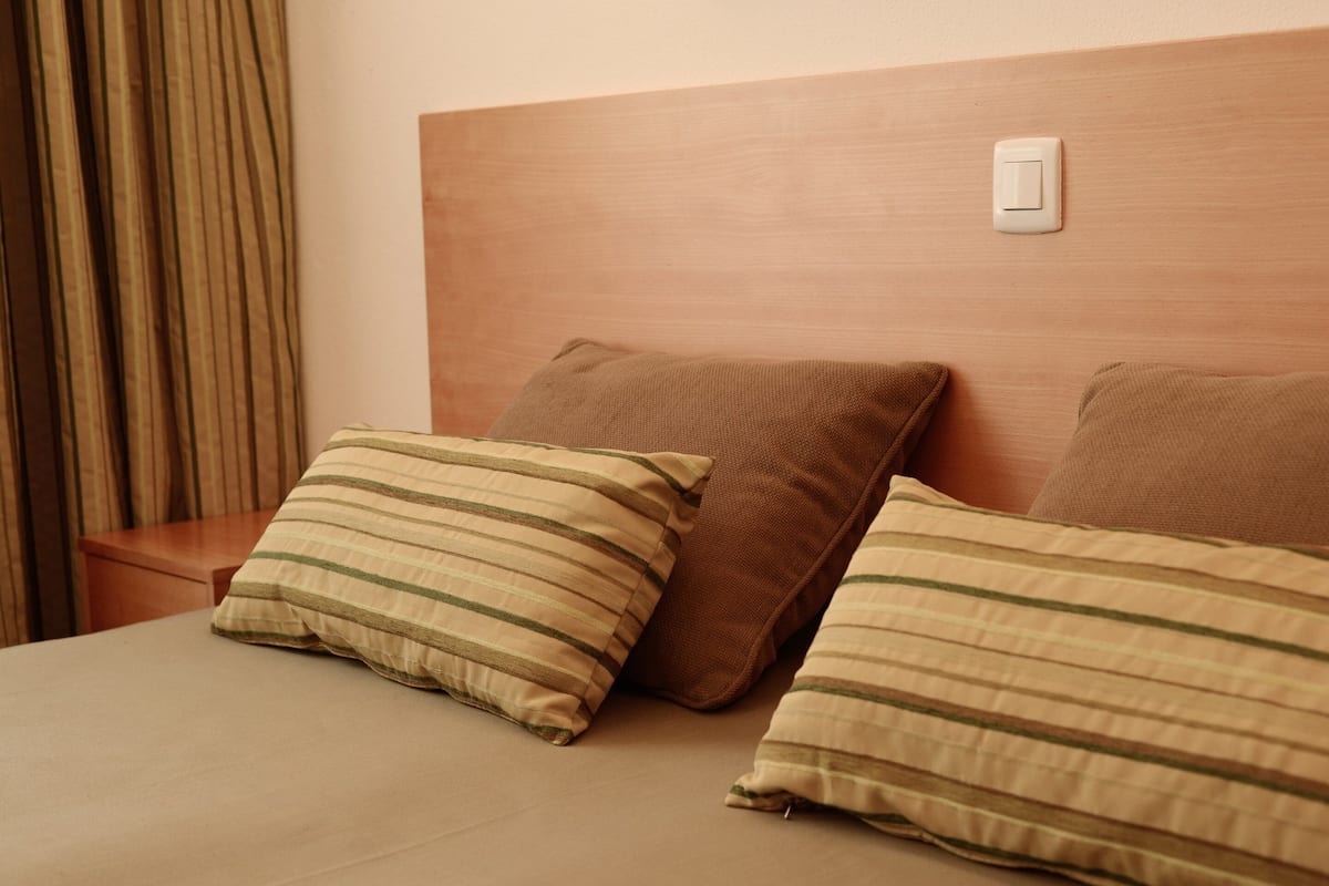 Una camera d'albergo con una testiera in legno, due cuscini e un comodino.