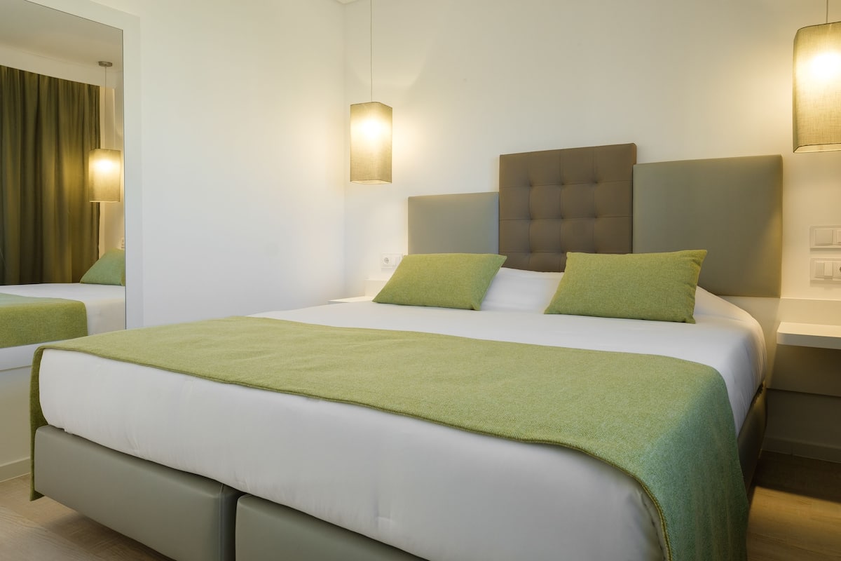 Una camera d'albergo moderna con un letto grande, un comodino e uno specchio.