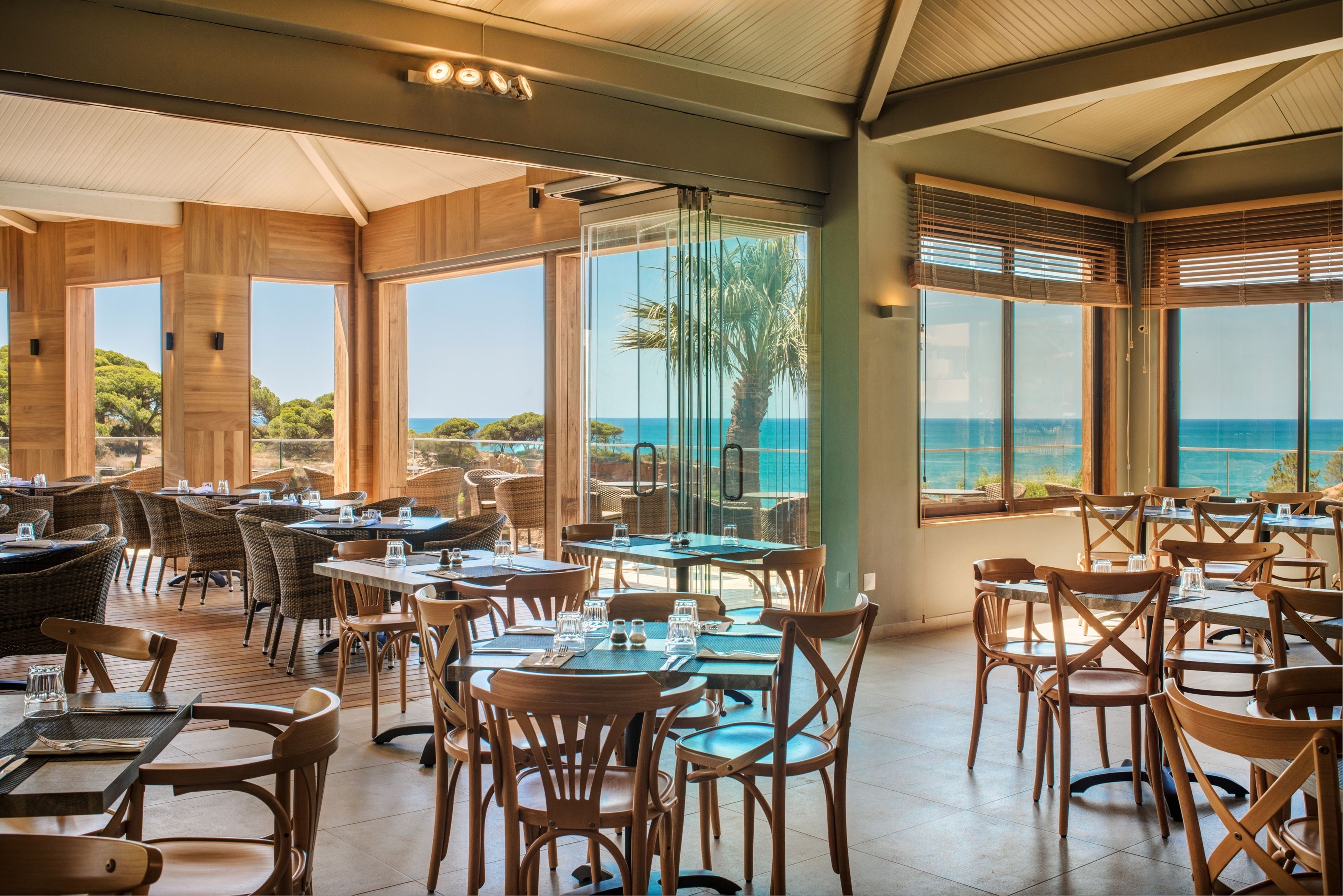 A restaurant with wooden furniture and large windows offering a view of the sea.