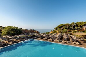 A poolside area with sun loungers and umbrellas, overlooking a body of water and a rocky coastline. - 3HB Falésia Garden (Albufeira)