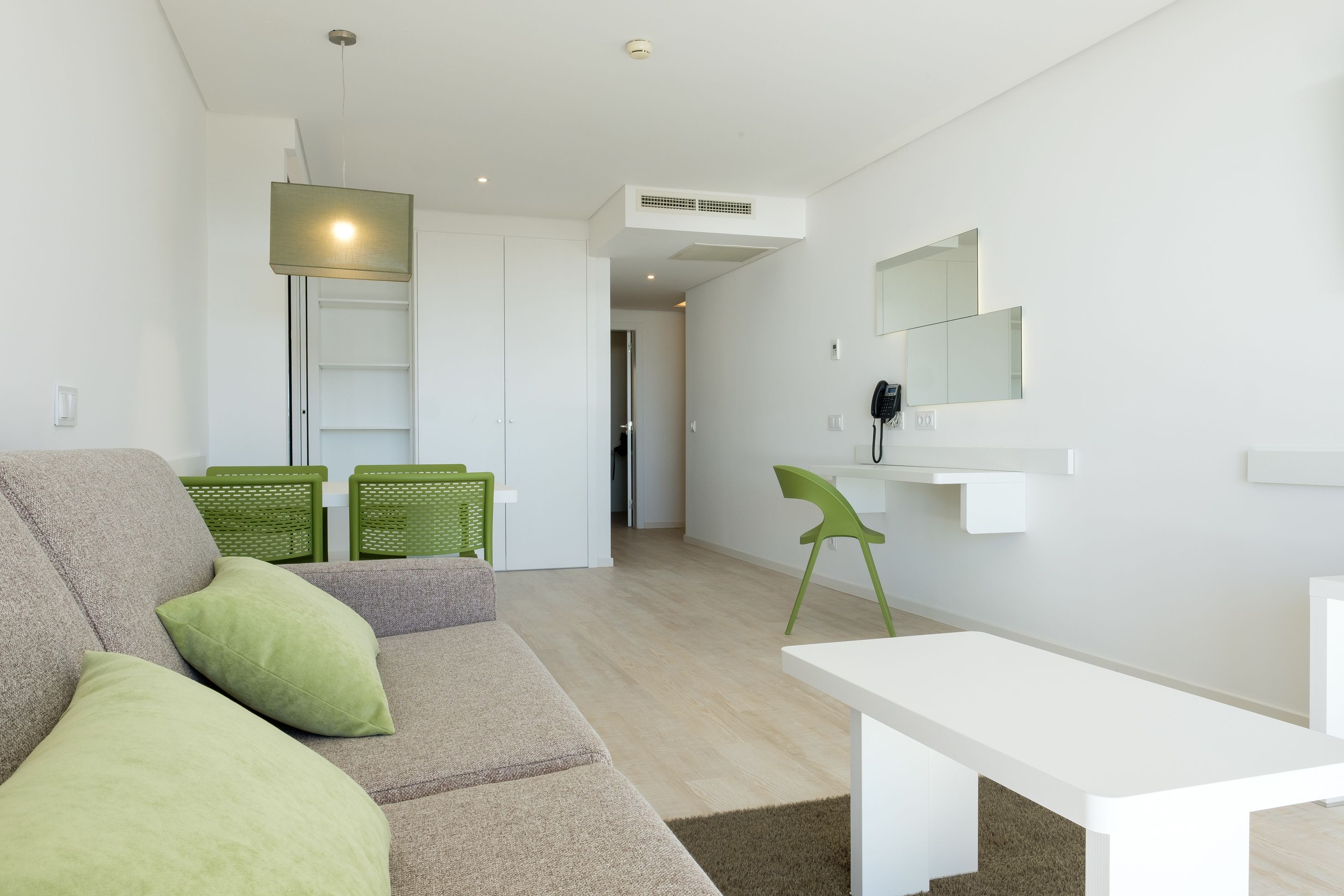 A modern living room with a grey sofa, green cushions, a white table, and a green chair.