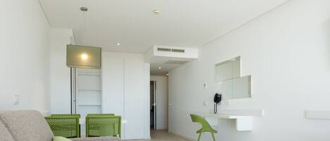A modern living room with a grey sofa, green cushions, a white table, and a green chair.