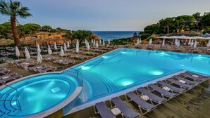 Ein Poolbereich mit Liegestühlen und Sonnenschirmen, eine Palme und Meerblick.