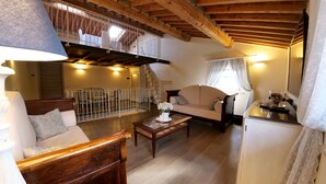 A cozy living room with a wooden ceiling, a sofa, a coffee table, and a staircase leading to an upper level. - B&B La Bella Lucca (Lucca)