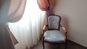 A room with a chair near a window with sheer curtains, a plain wall, and a wooden floor. - B&B La Bella Lucca (Lucca)