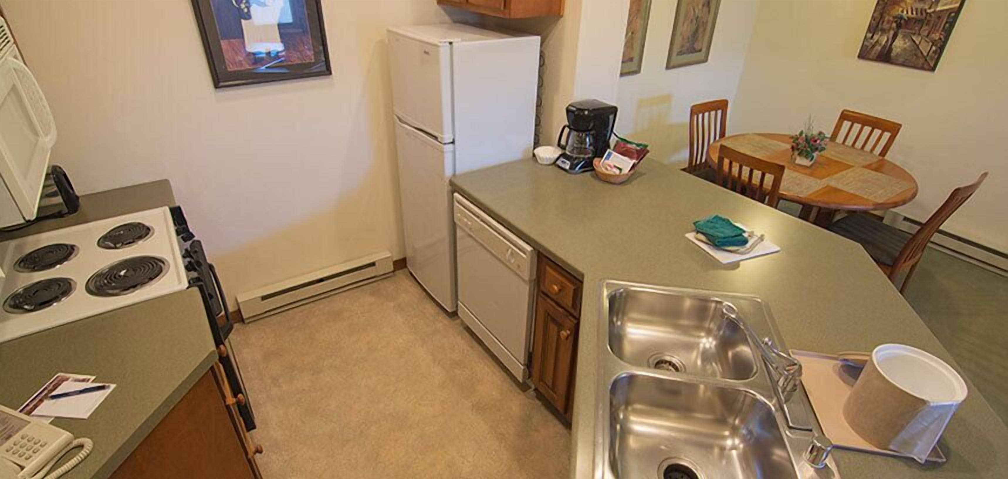 Una cocina compacta con estufa, refrigerador, cafetera y un comedor con mesa y sillas.
