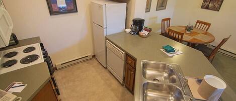 Una cocina compacta con estufa, refrigerador, cafetera y un comedor con mesa y sillas.