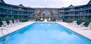 A swimming pool with lounge chairs and a building with balconies in the background. - Scandinavian Lodge (Sister Bay)