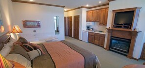 A bedroom with a large bed, a kitchen with wooden cabinets, a fireplace, and a TV. - Scandinavian Lodge (Sister Bay)