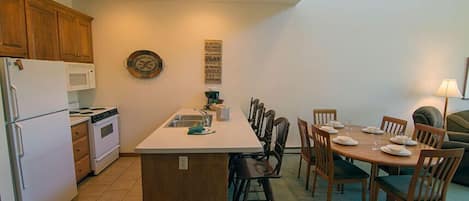 Une cuisine compacte dotée de meubles en bois, d’un four à micro-ondes, d’une cuisinière et d’un coin repas avec une table dressée pour quatre personnes.