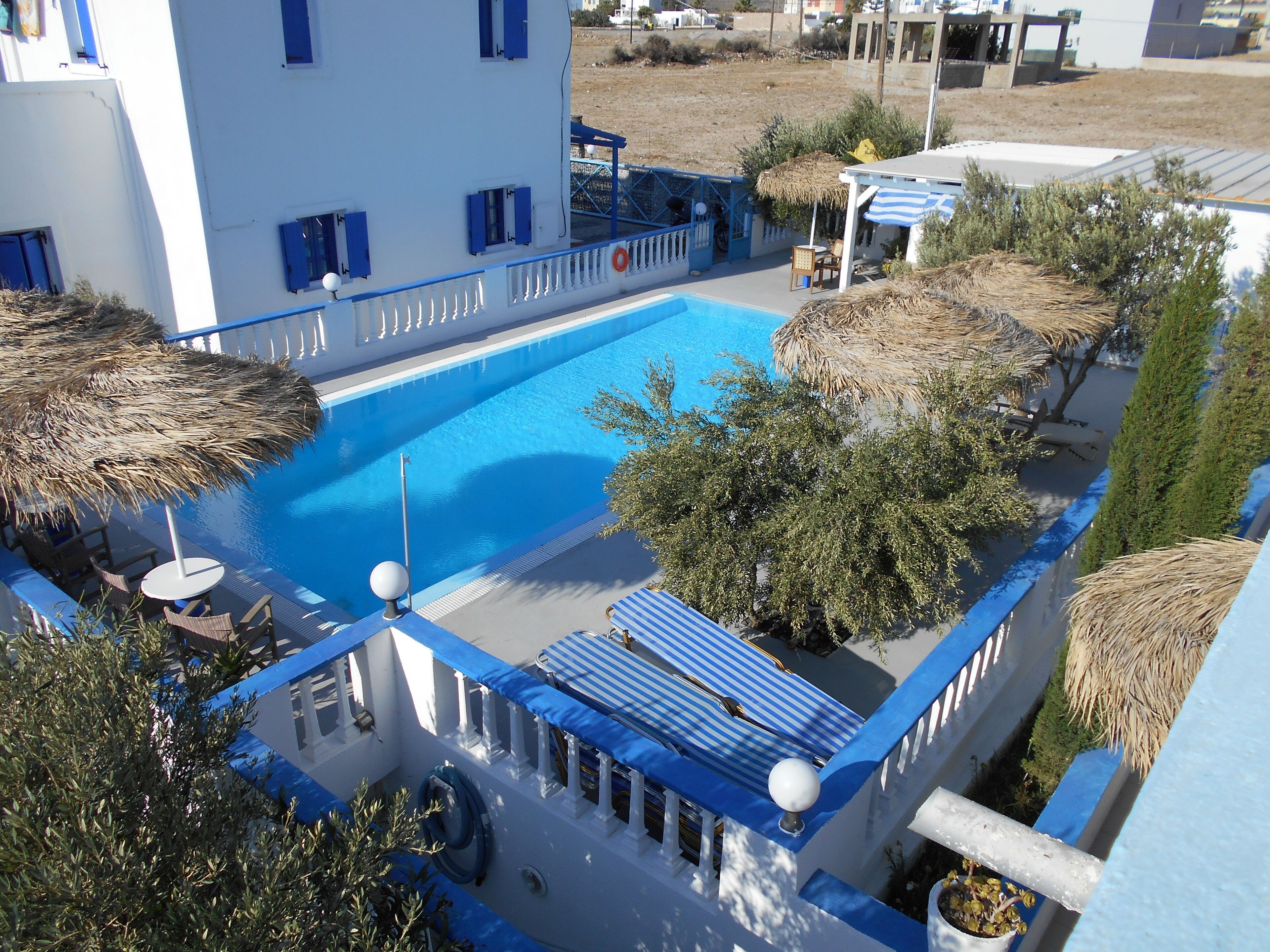 A pool area with a blue pool, white building with blue accents, and thatched umbrellas.