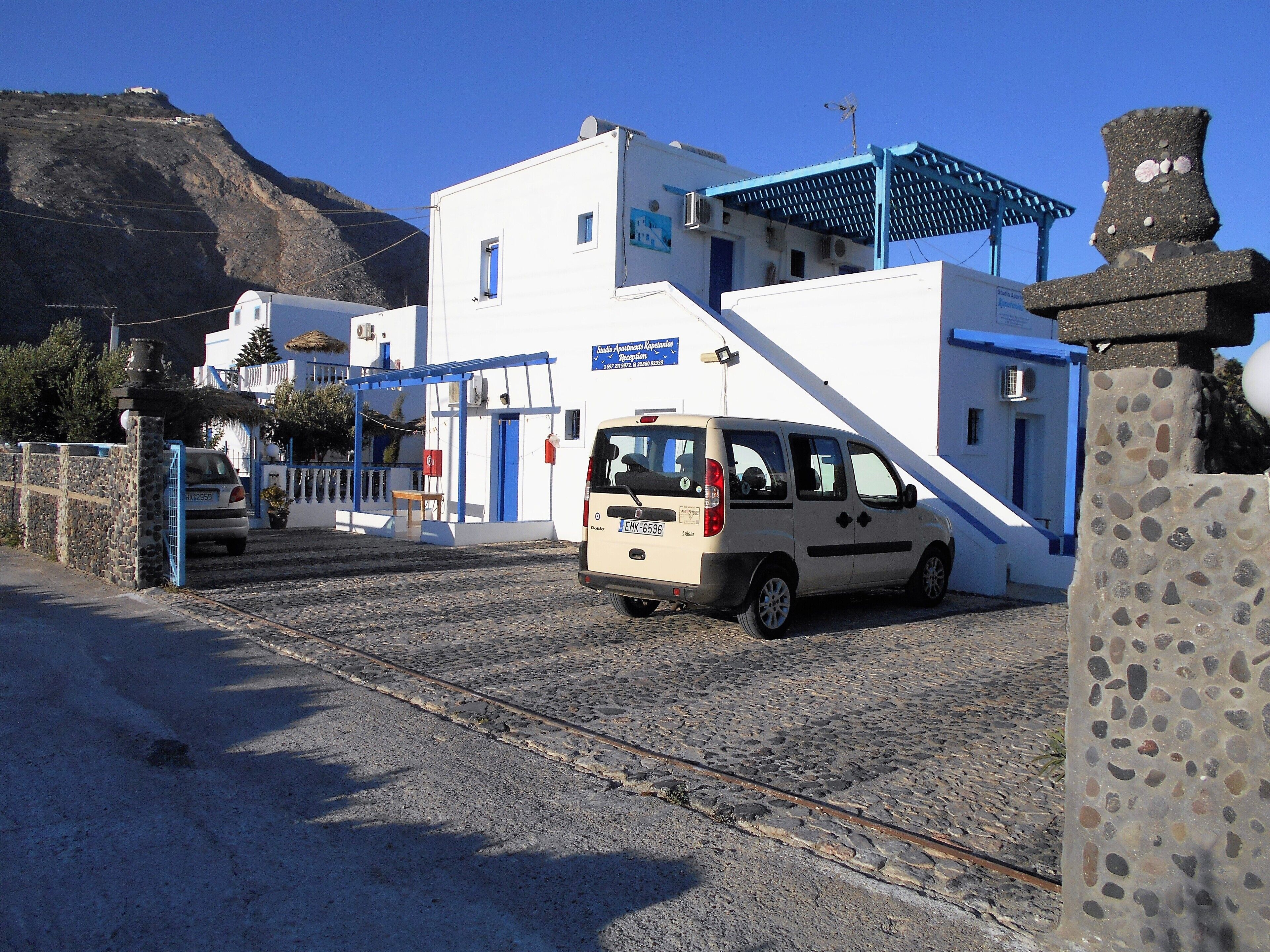 A building with a blue door and a white facade, a parked car, and a stone wall.
