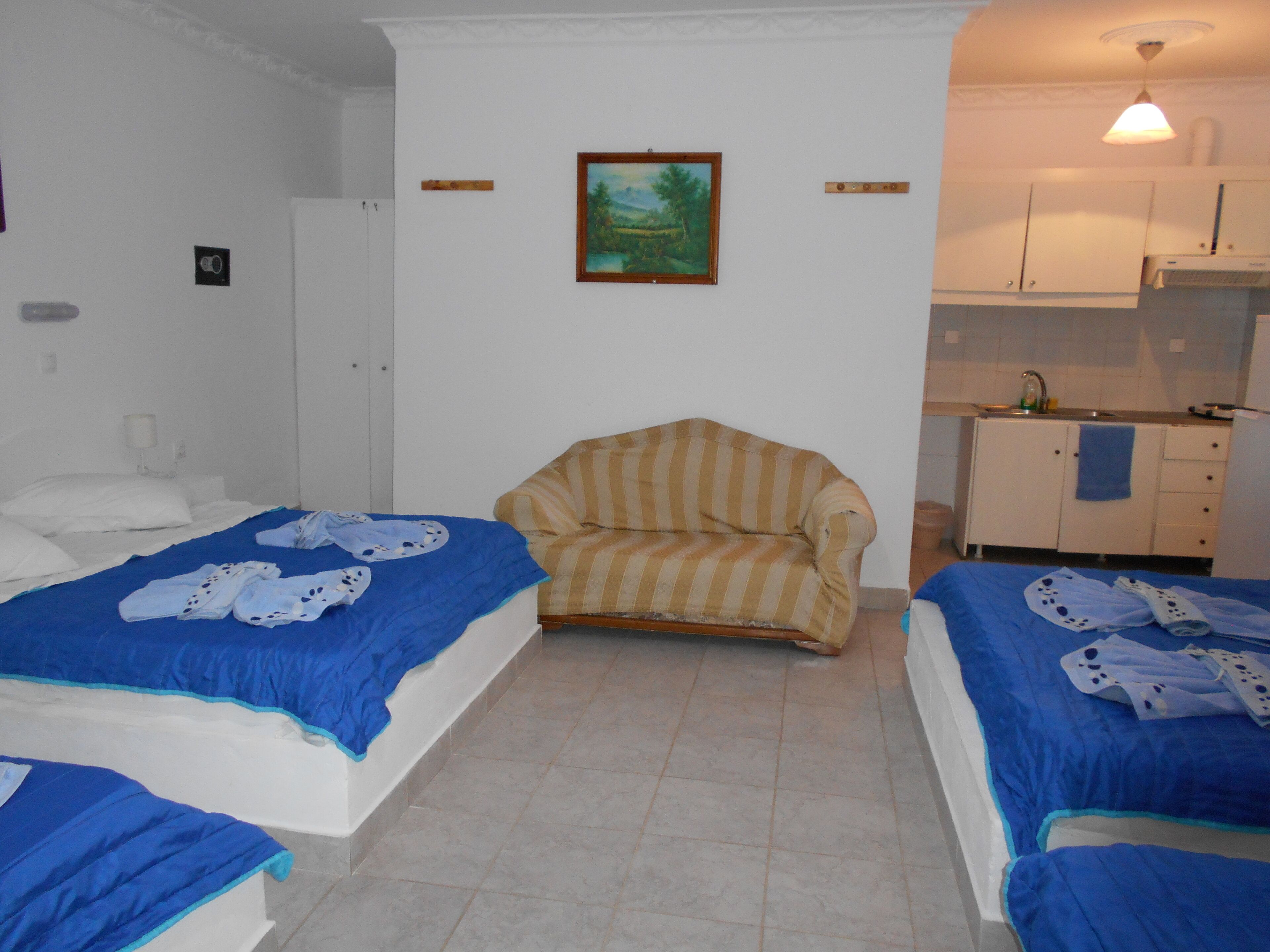 Una habitación con dos camas, una silla, un cuadro y una kitchenette.