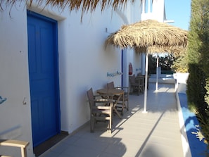 A patio with a blue door, a table with chairs, and a thatched umbrella. - Studios Apartments Kapetanios (Santorini)