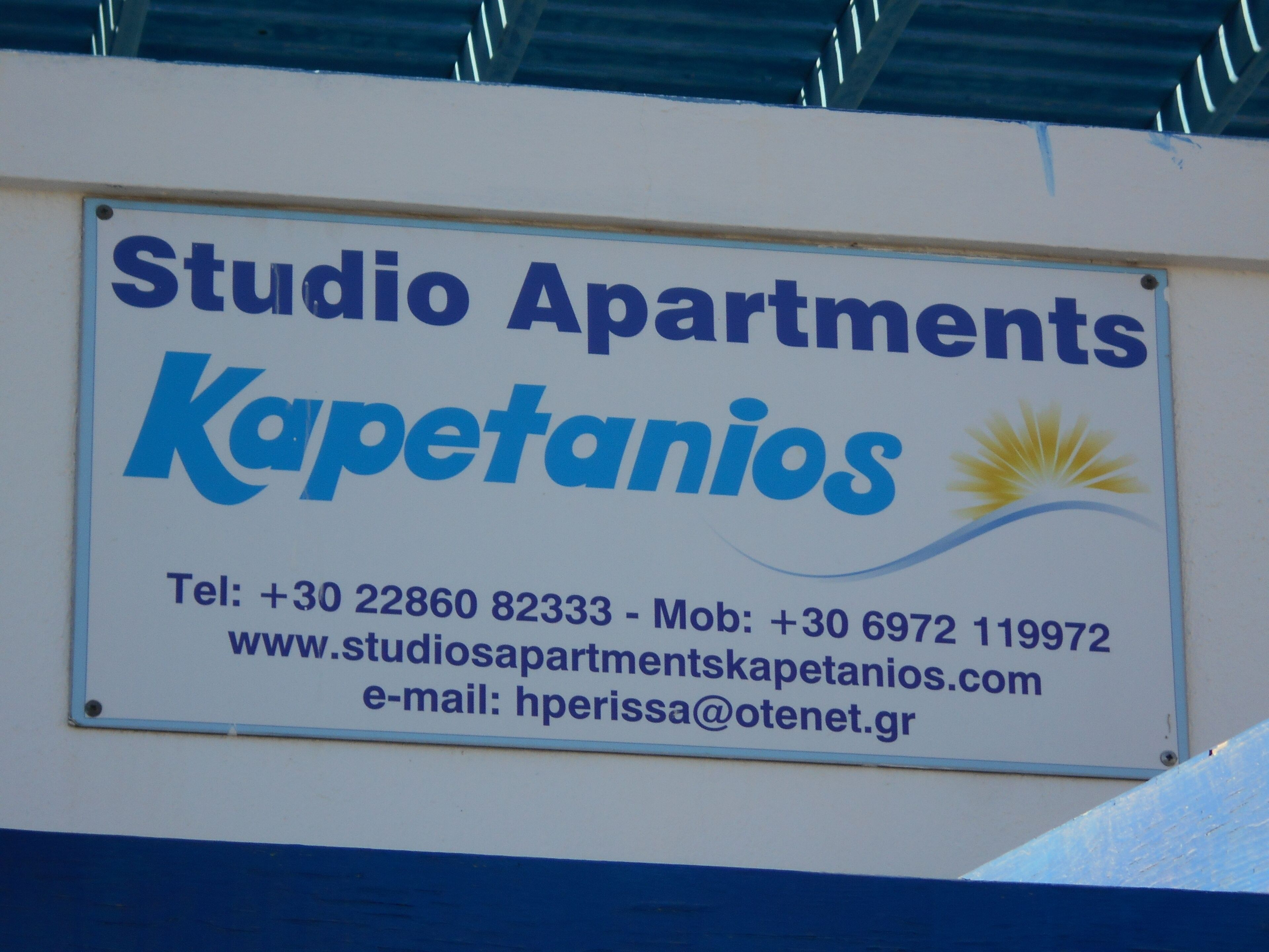 Letrero de Studio Apartments Kapetanios con información de contacto, incluyendo número de teléfono, número de móvil, sitio web y correo electrónico.